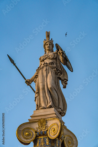 Statue of the Greek goddess Athena with spear and shield by Leonidas Drosis. Standing on a decorated Ionic column at the Academy of Athens, Greece – May 2025