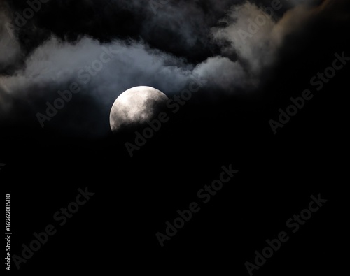Fotografia Mysterious full moon partially obscured by dark clouds in a night sky