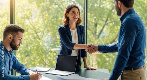 Smiling professionals shaking hands during a meeting, confirming agreement or hire while a colleague takes notes in sunlight.