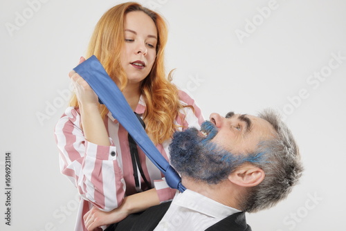 Young woman playfully strangling older bearded man by tightening his tie