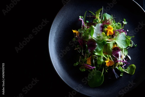 Fototapeta Naklejka Na Ścianę i Meble -  Verdant microgreens, delicate edible flowers cascading across dark ceramic plate, highlighting organic gourmet salad composition