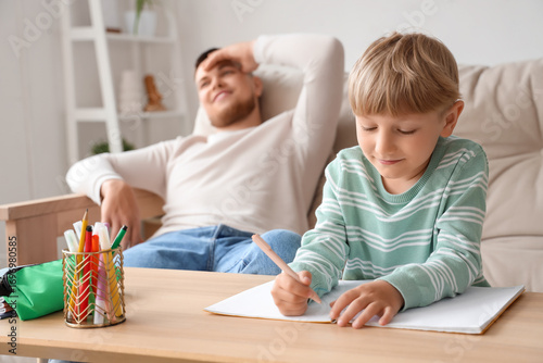 Father resting while his son doing homework in living room