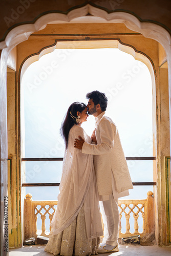 Foto Romantic Indian couple in elegant traditional white attire sharing an intimate moment under a historic archway, symbolizing love, culture, and heritage in India