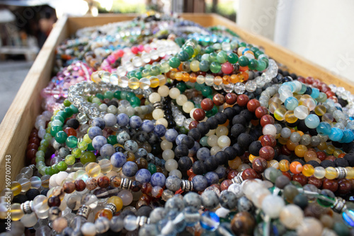 Rows of tumbled gemstones and crystals organized in clear trays at a store. Ideal for jewelry, geology, healing, craft supply, colorful background and retail display concepts.