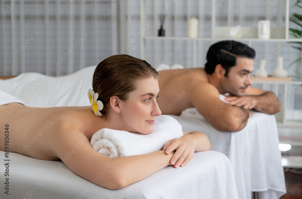 Naklejka premium Caucasian couple customer enjoying relaxing anti-stress spa massage and pampering with beauty skin recreation leisure in day light ambient salon spa at luxury resort or hotel. Quiescent