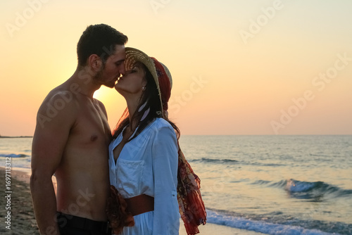 Happy young couple tenderly embracing and kissing at the beach at sunset.