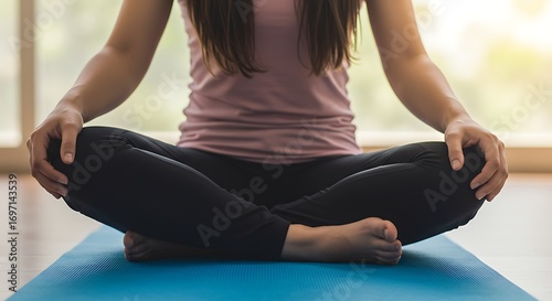 Person sitting cross-legged on yoga mat, hands resting on knees in meditation pose, soft natural light, no face visible