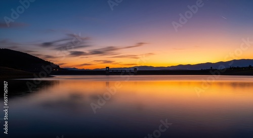 Serene sunset over a calm reservoir.  Silhouette of a dam against a vibrant  colorful sky.  Reflective water surface