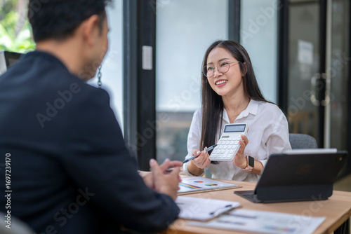 Asian businesswoman showing calculator to businessman during meeting