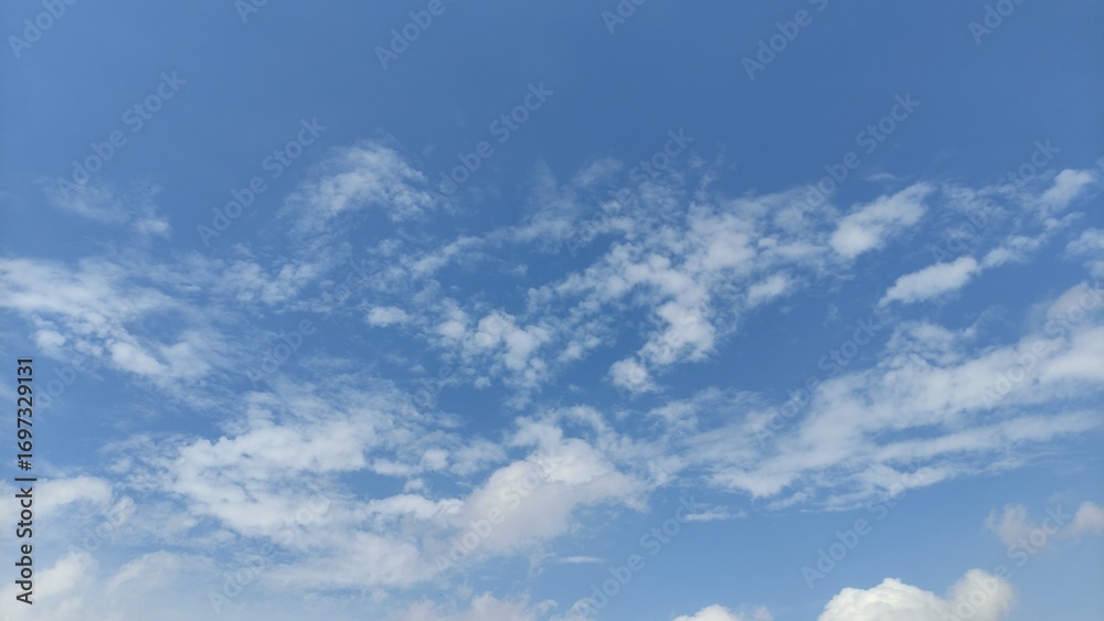 Naklejka premium Beautiful clear blue sky with scattered white clouds, symbolizing freedom, freshness, peace, and nature. Perfect for backgrounds, web design, posters, presentations, or educational materials