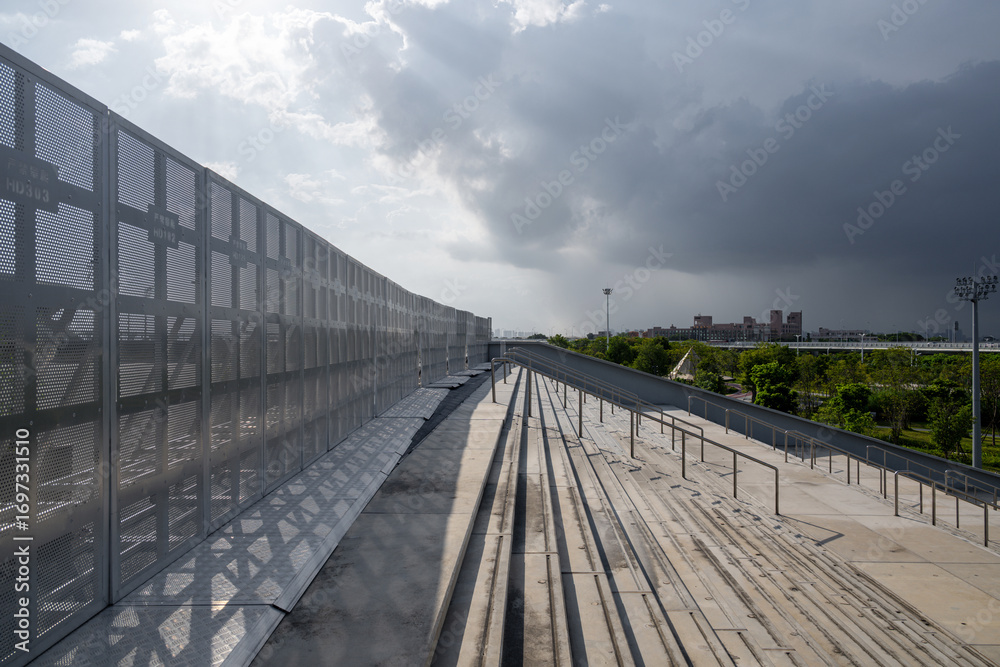 Fototapeta premium Metal Fence Along Elevated Railway Track Under a Stormy Sky in an Urban Setting
