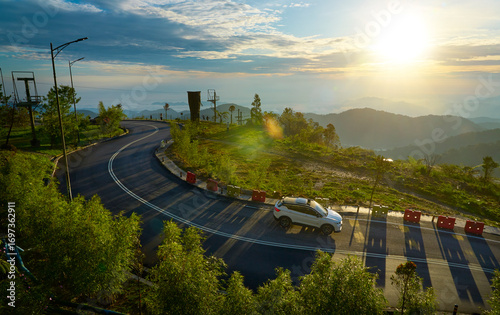 White suv driving on winding mountain road at sunrise