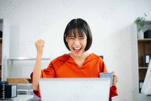 Joyful Asian woman celebrates a successful message while working in a bright office.