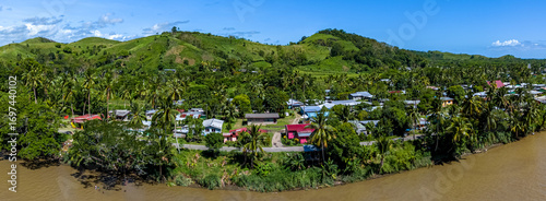 Panoramic aerial view of a traditional Fijian village with colorful houses nestled amongst palm trees on the banks of the muddy Sigatoka River, Fiji