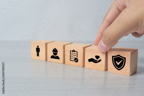 Safety at work concept. Hand holds cubes wooden block with safety icons; safety first, protections, health, regulations and insurance. Used for banner, beautiful bright background and copy space