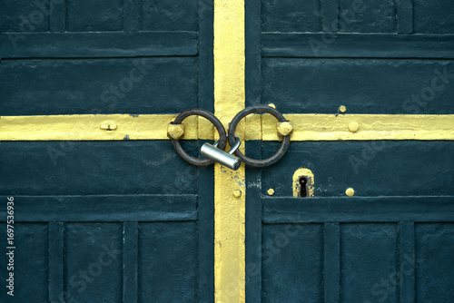 Fotografie Locked wooden door with yellow painted accents, two iron rings, and a metal padlock securing the entry