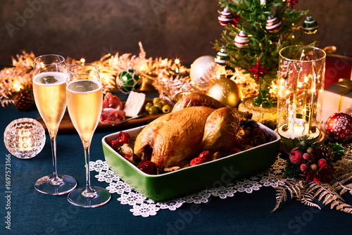 クリスマスツリーとイルミネーションに囲まれた食卓にローストチキンとシャンパンが並ぶ華やかなホリデーディナー　家族やカップルの祝宴をイメージさせる温かい雰囲気