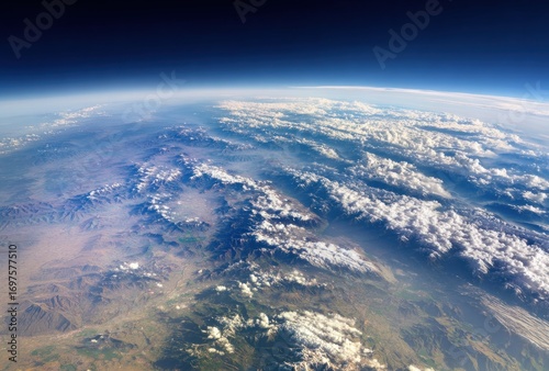 Stunning view of Earth from space, featuring a curved horizon, clouds, and mountains. Bright blues & earthy tones dominate