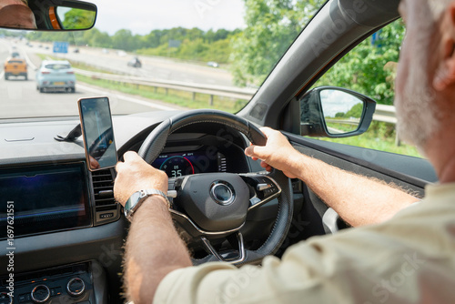 Driving on a sunny day with the hands on the steering wheel and mobile phone mounted for navigation and updates on a highway in the countryside