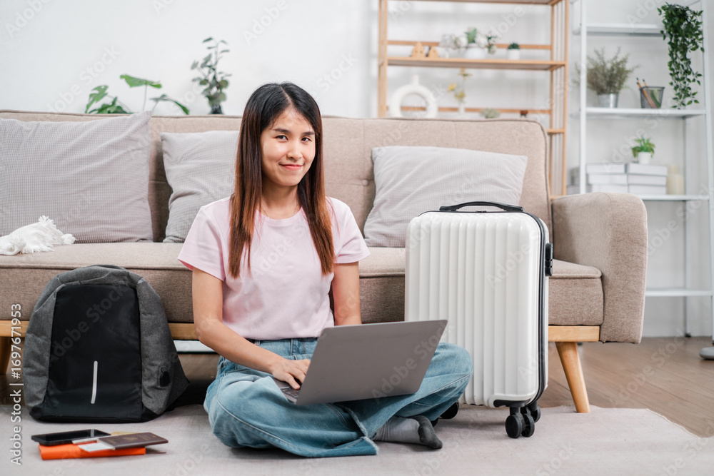 A young woman sits on the floor with a laptop, surrounded by luggage and a backpack, ready for travel in a cozy living room. A young woman sits on the floor with a laptop, surrounded by luggage and a backpack, ready for travel in a cozy living room.