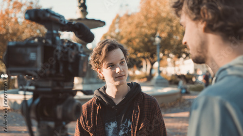 A short interview outdoors: a cameraman with a camera and a young interviewee in the frame, a documentary atmosphere.