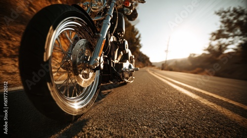 A low angle shot of a motorcycle on an asphalt road, trees on the sides, and bright sunlight in the distance, with a blurred background