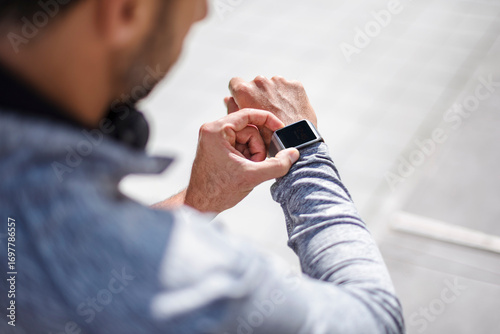 Man in sportswear checking smartwatch during running break in city