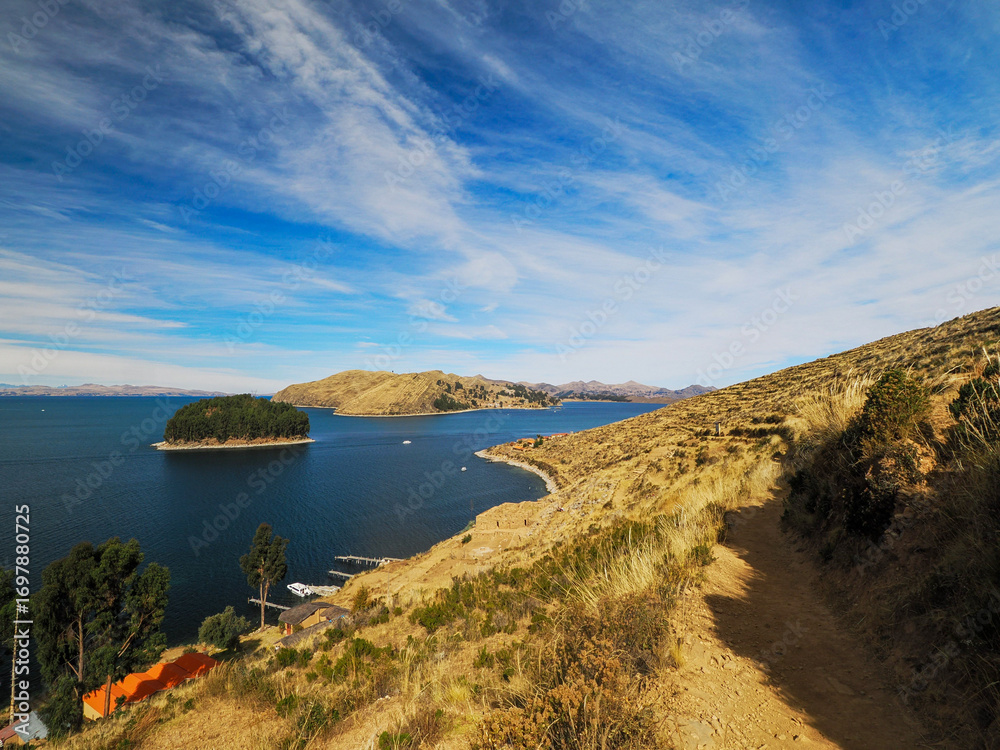 Obraz premium Picturesque landscape of Isla del Sol on Titicaca Lake in Bolivia. Yellow dry vegetation, deep blue lake, blue sky with gentle white clouds.