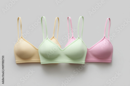 Four pastel-colored soft bras with thin straps are placed in a row against a light gray background for lingerie advertising.