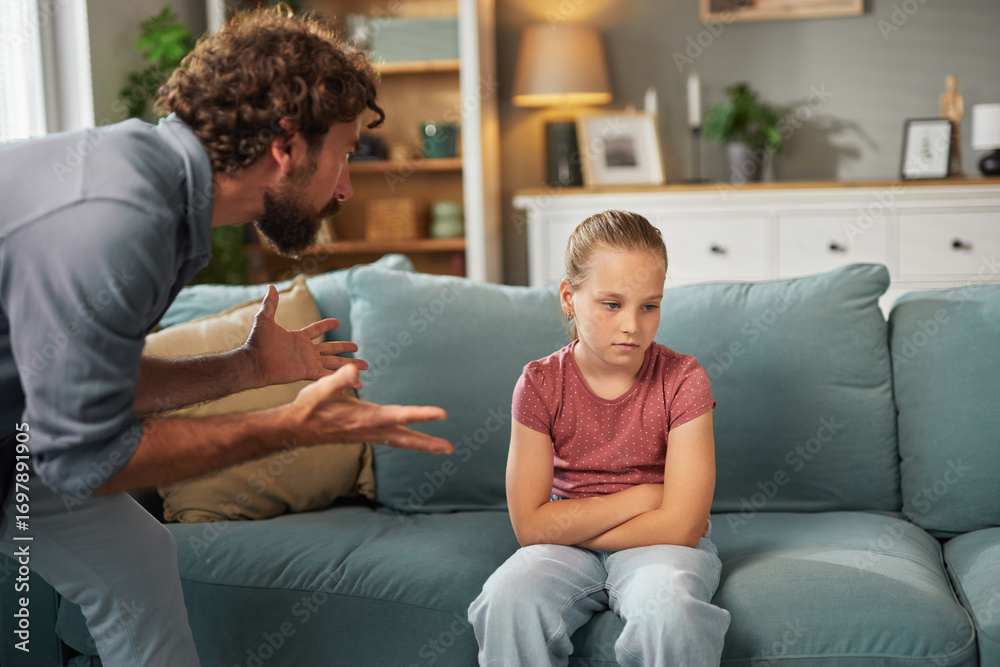 Obraz premium A father is talking to his daughter who looks upset while sitting on a couch at home. The atmosphere hints at a recent disagreement, with clear signs of tension in their expressions.
