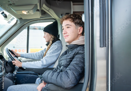 Teen boy enjoying the ride in campervan next to his sister who is driving, peaceful moment during road trip adventure