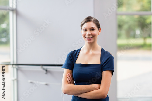 Free Download Smiling woman in twenties standing in lobby near large glass window pane and frame, arms crossed - GFXLoad