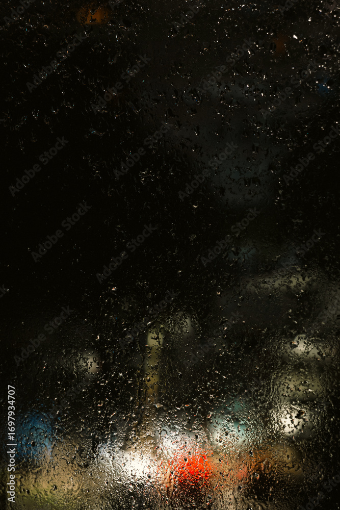 Fototapeta premium Rainy Night Cityscape Through Wet Window with Copy Space and Cinematic Mood. Rain-covered window, with water droplets and blurred city lights in the background. Soft bokeh and diffused lightting.