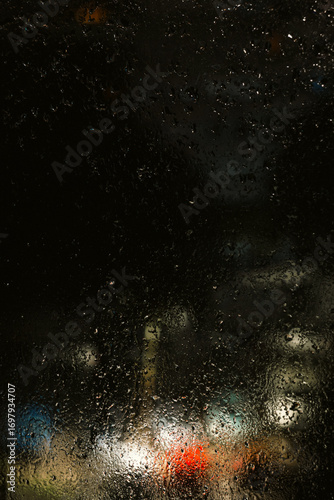Rainy Night Cityscape Through Wet Window with Copy Space and Cinematic Mood. Rain-covered window, with water droplets and blurred city lights in the background. Soft bokeh and diffused lightting.