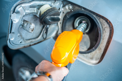 Close up of gas station worker holding blue fuel pump, filling orange sports car tank. Automotive refueling, petrol station service, and transportation concept in vibrant outdoor.