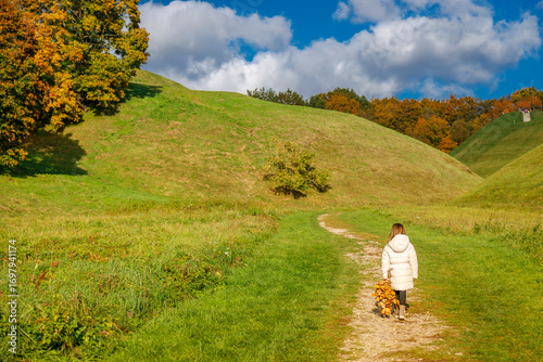 Wallpaper Mural A girl walking along a winding path in a scenic green valley during autumn Torontodigital.ca
