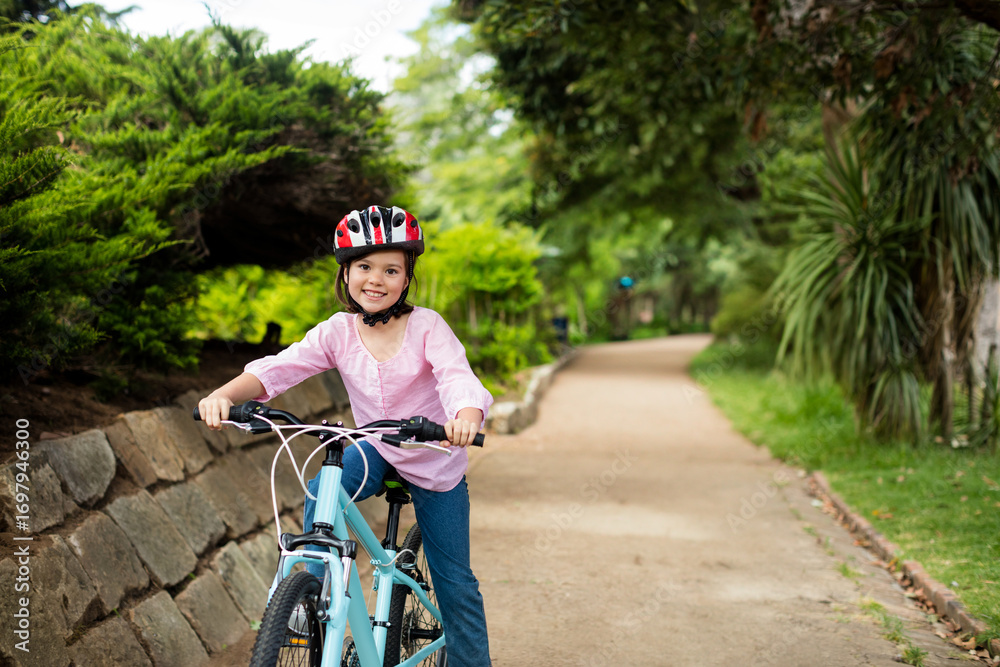 Naklejka premium Light blue bicycle is resting on dirt path in park, bordered by stone wall and shrubs