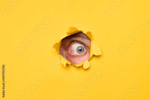 Human eye looking through torn yellow paper