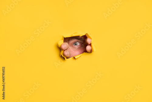 Curious man looking at camera through torn yellow paper