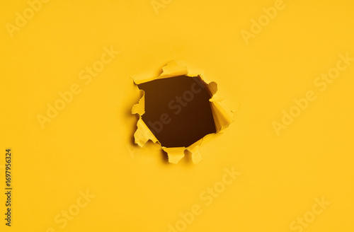 Torn hole in yellow paper with dark background.