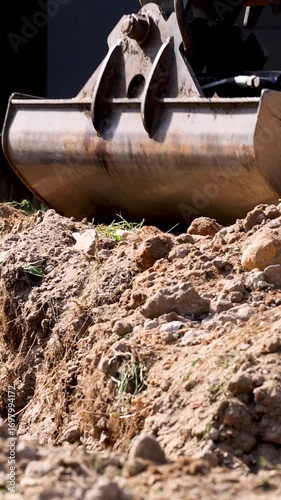 Excavator bucket filling trench with soil in vertical format