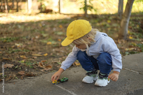 Photography Three-year-old boy squatting and playing with toy cars outdoors
