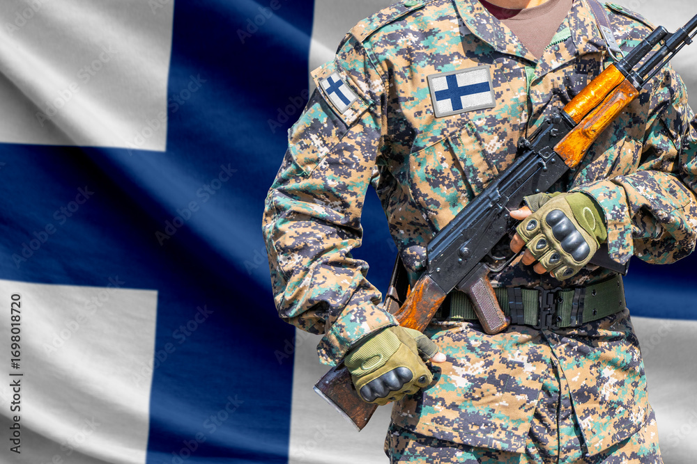 Fototapeta premium Finland flag with soldier in military uniform holding assault rifle in front of it