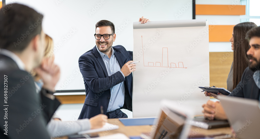 Businessman standing at whiteboard drawing and presenting diagrams to colleagues Businessman standing at whiteboard drawing and presenting diagrams to colleagues