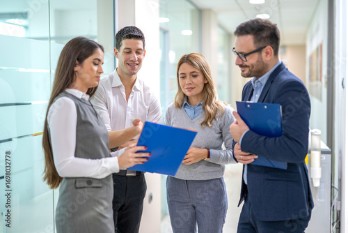 Tableau sur toile Four business people standing in office hallway discussing report during impromp