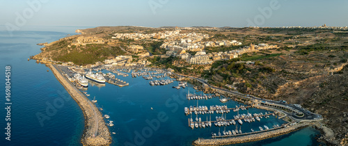 Aerial view of Mgarr Harbour where yachts bob gently in the turquoise water, overlooked by the town's sandstone buildings, Gozo, Malta.