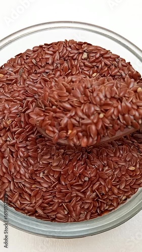 Taking out a spoonful of organic Flaxseeds with a wooden spoon from a glass bowl on a white background, top view, Dry Linum usitatissimum, vertical clip