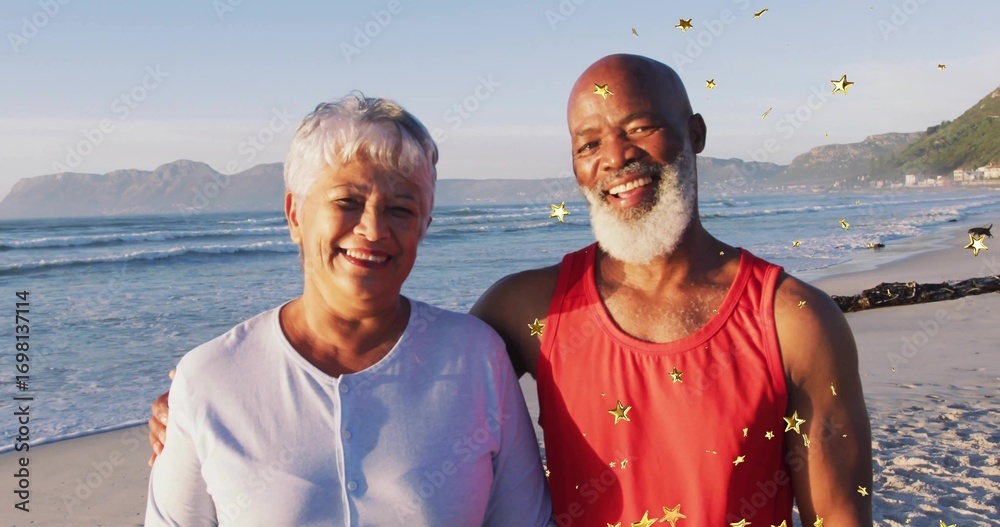 Fototapeta premium Smiling couple in red shirt and light cardigan posing on sandy beach, with golden confetti