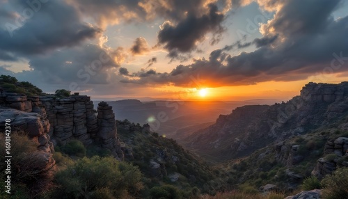 Dramatic sunset paints the sky with vibrant orange and yellow hues over a deep canyon landscape