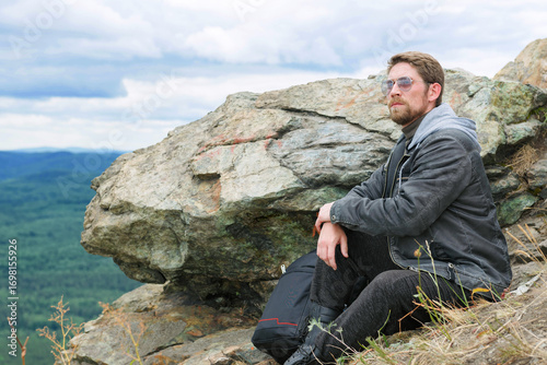Man in a gray jacket is sitting on a mountain top.